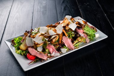 Renkli ve taze salata ve ördek göğsü ve peyniri. Bir parça ördek filetosu ve salata. Şirket için bir tabak. Fotokopi alanı için siyah arka plan.