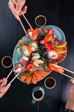 Bir Japon restoranında ahşap bir masanın üzerinde bir suşi seti. Suşi ve saşimi çubukların üzerinde, arkadaşlar Japon restoranının üst manzarasında rulo ekmek yiyorlar. Arkadaşlar ve aile suşi yiyor.