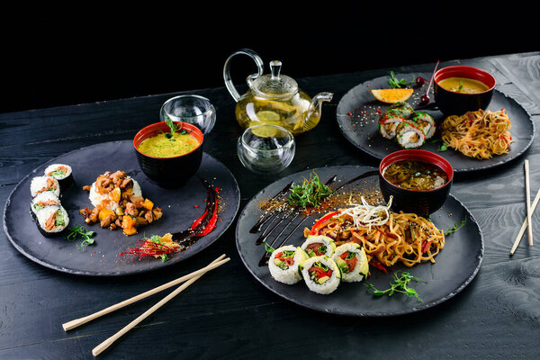 Традиционные японские блюда - суши, роллы, рис и удонскую лапшу на тёмном фоне. Вид сверху на азиатскую еду, подаваемую на стол большой набор. Китайская, японская и вьетнамская кухня