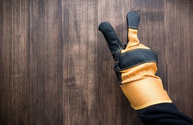 İnşaat eldivenleri ahşap arka planda zafer işareti gösteriyor, yakın çekim, üst görüş, kopyalama alanı