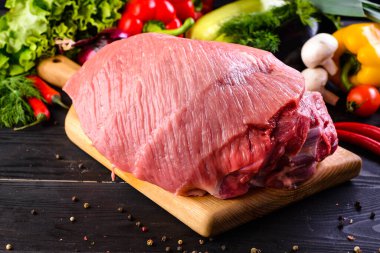 Büyük bir parça çiğ domuz eti. Kalça, kalça ya da fileto. Siyah ahşap arka planda sebze ve baharatlı.