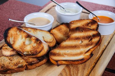 Ahşap plaka üzerinde kızarmış ekmek ile farklı sos.