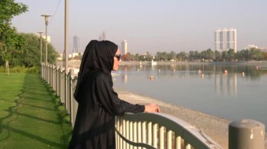 Müslüman Arap genç ve güzel bir kadın Dubai, BAE 'deki Barsha parkında suya bakıyor..