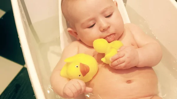 Bébé fille drôle tient canards en caoutchouc dans une baignoire — Photo