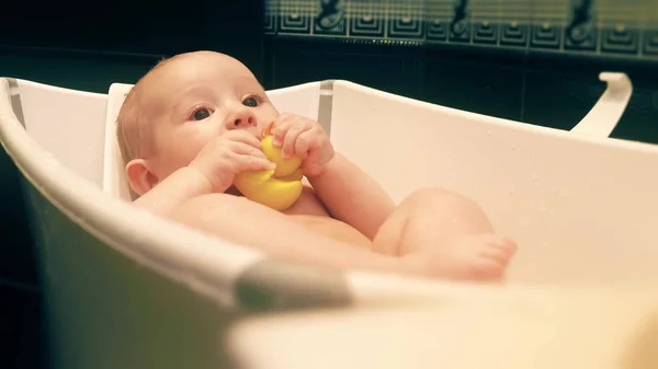 Bébé fille tient canard en caoutchouc dans une baignoire — Photo