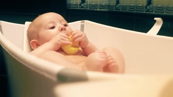 Babymeisje houdt rubber eend in een badkuip — Stockvideo
