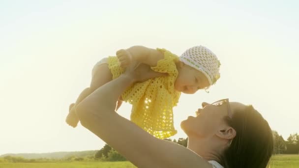 Mamma felice che tiene la sua bambina sorridente contro il sole splendente — Video Stock