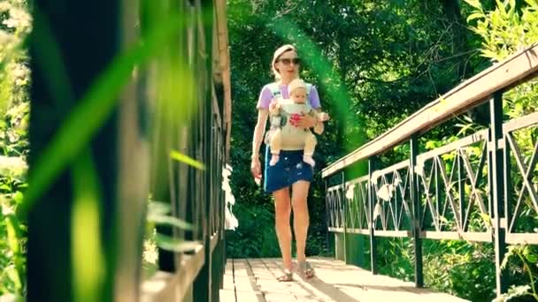 Schöne junge Frau trägt ihr Kind in einer Tragetasche — Stockvideo