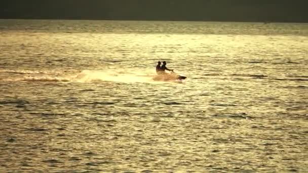 Dos personas montando moto acuática en el mar al atardecer. Disparo en cámara lenta — Vídeo de stock