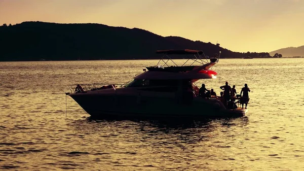 Неизвестные устраивают вечеринку на борту моторной яхты в море на закате — стоковое фото