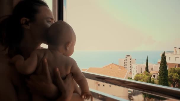 Mutter und ihr kleines Baby blicken im Urlaub aus dem Fenster aufs Meer — Stockvideo