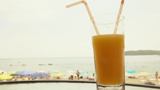 Bicchiere di succo d'arancia fresco contro la spiaggia sfocata — Video Stock