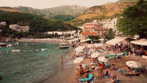 MILOCER, MONTENEGRO - 1 de agosto de 2018. Pequeña playa llena de gente por la noche — Vídeos de Stock