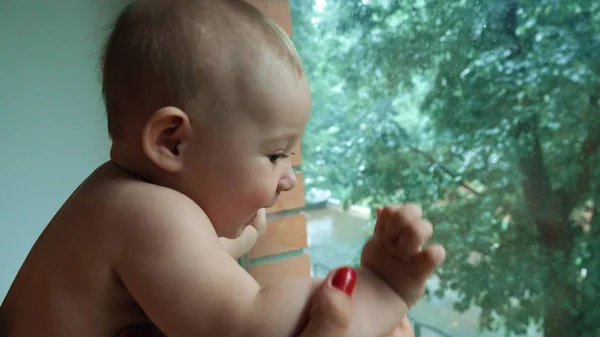 Bébé heureux regardant la pluie derrière la fenêtre de la maison — Photo