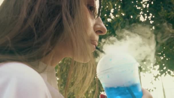 Genç kadın bir sıcak yaz gününde mavi kuru buz içki sigara sahip — Stok video