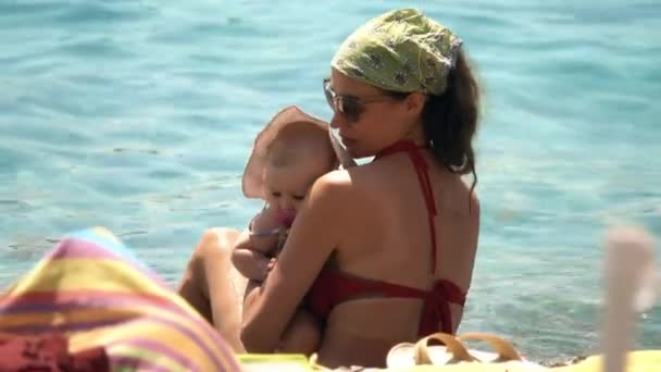 Мама держит свою маленькую дочь на руках на пляже — стоковое видео