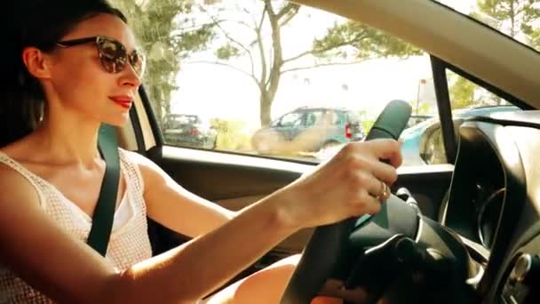 Όμορφη νεαρή γυναίκα που φοράει γυαλιά ηλίου οδηγεί ένα αυτοκίνητο σε μια ηλιόλουστη καλοκαιρινή μέρα — Αρχείο Βίντεο
