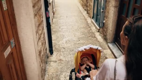 Мать с ребенком прогуливаются по старому городу Монтенегро с коляской — стоковое видео