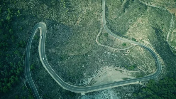 Vista aérea de cima para baixo de uma estrada de carro ventoso em montanhas — Fotografia de Stock