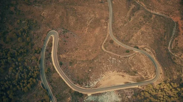 Vista aérea de arriba hacia abajo de un coche que se mueve a lo largo de la carretera ventosa en las montañas — Foto de Stock