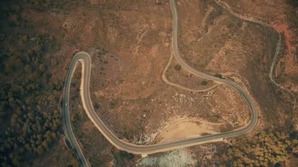 Vista aérea de arriba hacia abajo de un coche que se mueve a lo largo de la carretera ventosa en las montañas — Vídeos de Stock