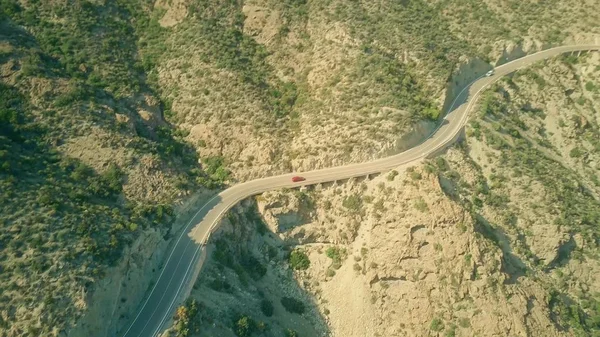 Veduta aerea di una macchina rossa che si muove lungo la strada ventosa in montagna — Foto Stock