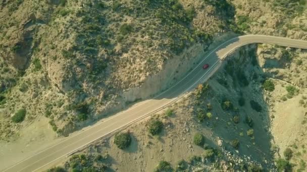 Вид з повітря на червоний автомобіль, що рухається по вітряній дорозі в горах — стокове відео