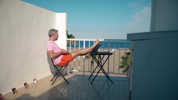 Happy freelancer finishes his works on laptop while sitting on seaview terrace — Stock Video