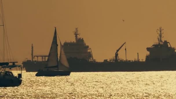 GIBRALTAR, GREAT BRITAIN - SEPTEMBER 27, 2018. Silhouette of maneuvering sailboat and distant cargo ships at sunset — Stock Video