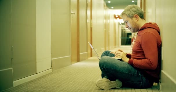 Homem de cabelos grisalhos inteligente em roupas casuais usa seu laptop no corredor do hotel — Vídeo de Stock