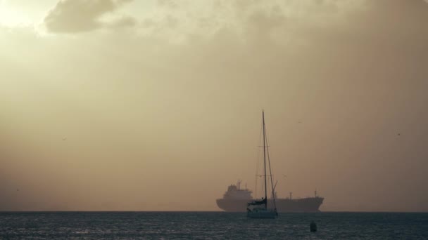 Zeilboten tegen vrachtschip bij zee zonsondergang — Stockvideo