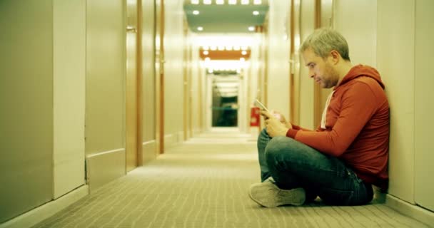 Сіра волохата людина в повсякденному одязі, використовуючи свій смартфон в готельному коридорі — стокове відео