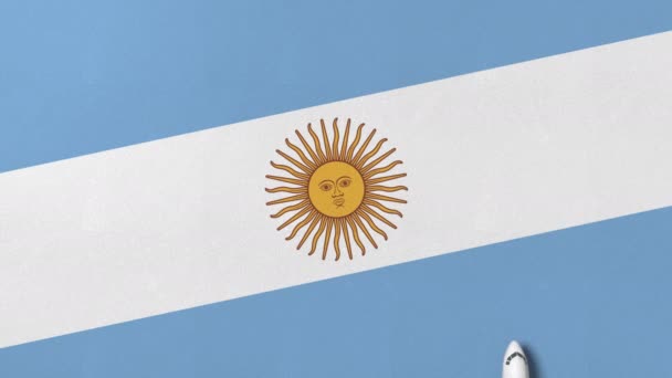 Vista de arriba hacia abajo del avión en la bandera de Argentina. Animación 3D conceptual relacionada con el turismo — Vídeo de stock