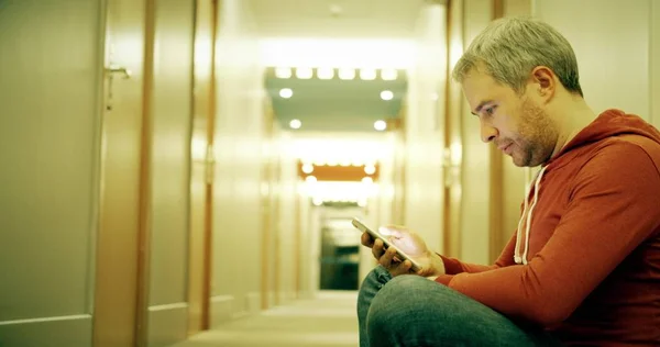Handsome man in casual clothes uses his smartphone in the hotel hallway — Stock Photo, Image