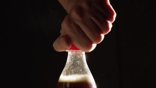Человек открывает пластиковую бутылку пенной колы на черном фоне — стоковое видео