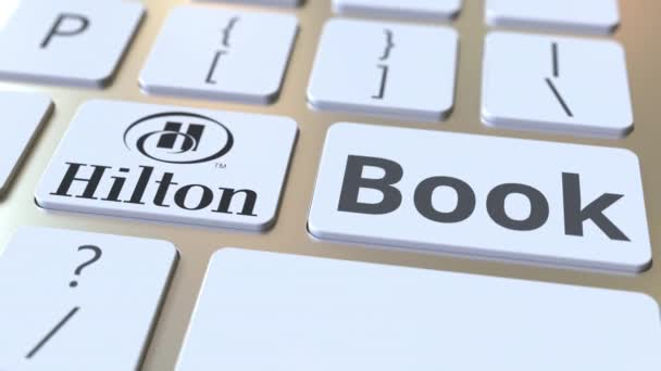 Logo firmy Hilton i tekst książki na klawiszach klawiatury komputerowej, redakcyjnej animacji koncepcyjnej — Wideo stockowe