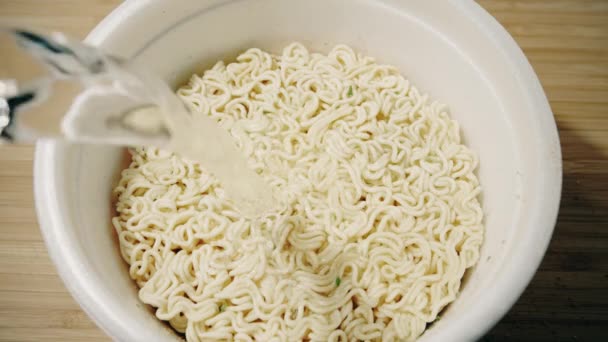 Pouring some water into cup with instant noodles, down view. Slow motion shot — Stock Video