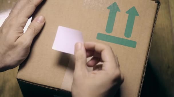 Man sticks a white sticker label to parcel carton box. Place for revealing text or logo — Stock Video