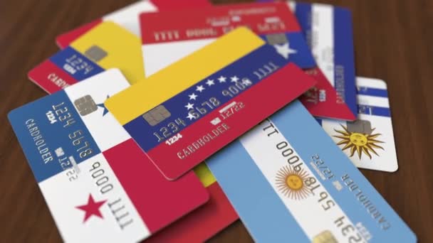 Viele Kreditkarten mit verschiedenen Flaggen, hervorgehobene Bankkarte mit venezuelaer Flagge — Stockvideo