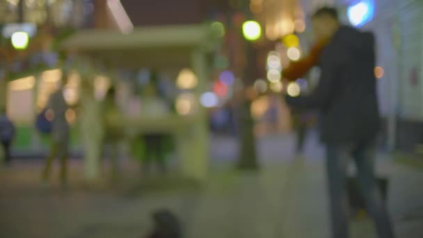 Неизвестный уличный музыкант вечером играет на электрической скрипке в освещенной пешеходной зоне — стоковое видео