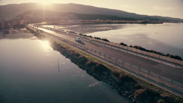 Flygbild av okänd bil och cyklist som rör sig längs dammen till sjöss på kvällen. Orbetello, Italien — Stockvideo