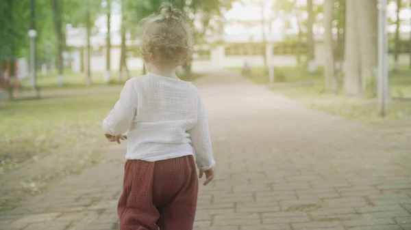 Σγουρά ξανθιά μωρό κορίτσι περπατάει στο πάρκο μια καλοκαιρινή μέρα — Φωτογραφία Αρχείου