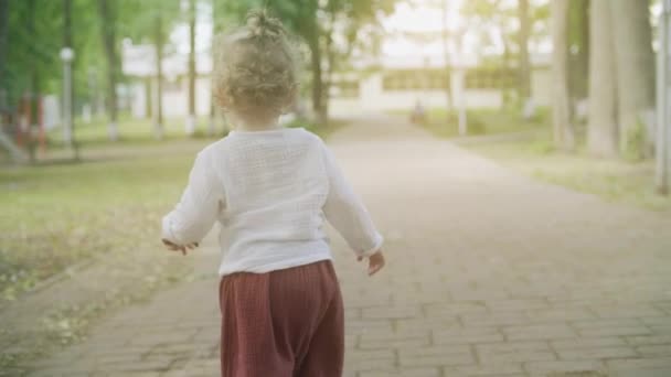 Bouclé blonde bébé fille marche dans le parc un jour d'été, tir au ralenti — Video