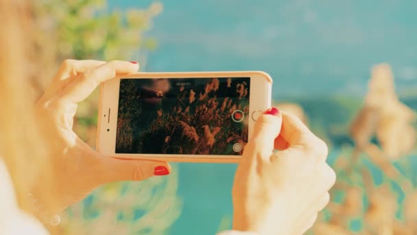 Mujer joven filmando vídeo de paisaje con su teléfono inteligente en la orilla del lago. Disparo en la cámara roja — Vídeos de Stock