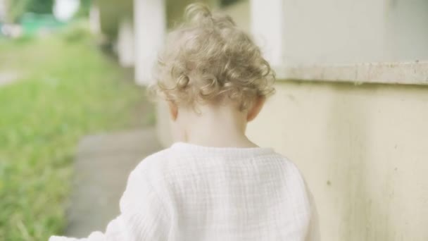 Krullend blond baby meisje wandelen, close-up geschoten van de rug — Stockvideo