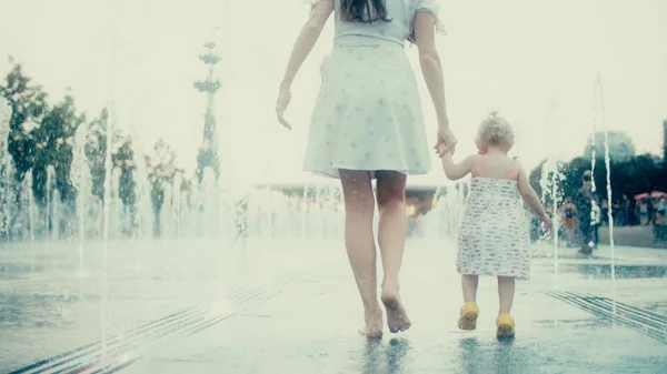 Мама и ее маленькая дочь ходят в фонтане, держа за руки, замедленный выстрел — стоковое фото