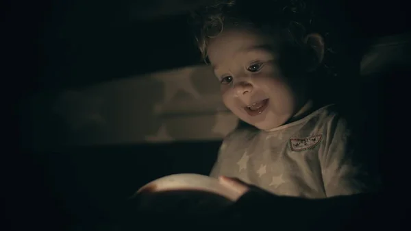 Bebê pequeno feliz olha para brinquedo projetando luminoso no quarto escuro — Fotografia de Stock