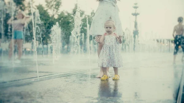 Mãe e seu pequeno bebê se divertindo na fonte do parque da cidade, câmera lenta — Fotografia de Stock