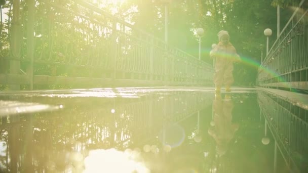 Happy Little Baby in oranje Waterdichte regenjas en rubber regen laarzen loopt op plas na regen, Slow Motion — Stockvideo