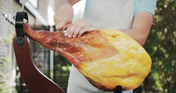 Un uomo inizia a tagliare tutta la gamba di Jamon. Girato su Rosso — Video Stock